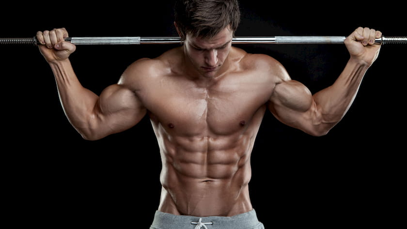 man with no shirt on holding barbell behind his back